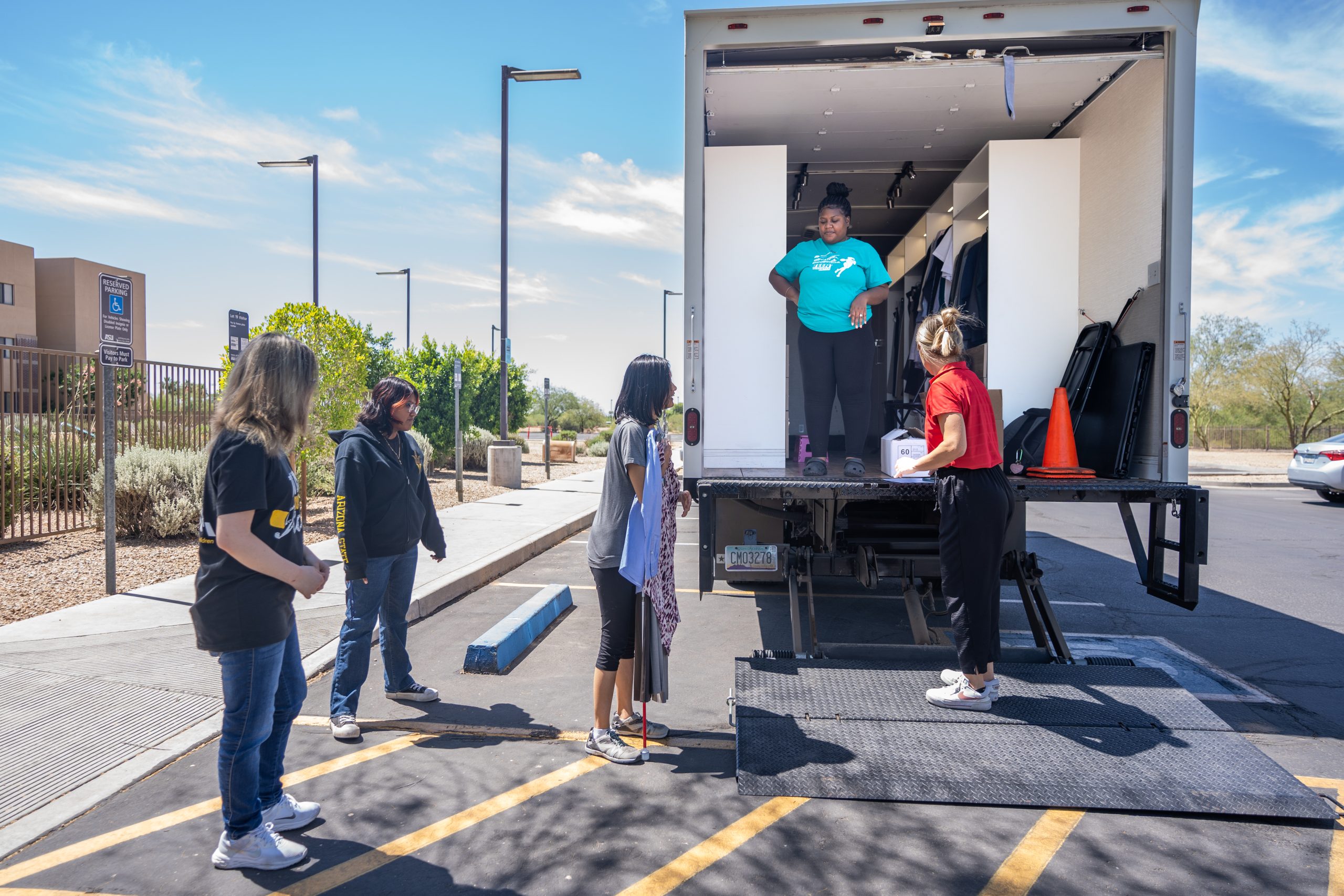 Teens standing outside a truck on the ASU campus, engaged in a hands-on dress for success activity with a mobile closet setup inside the truck.