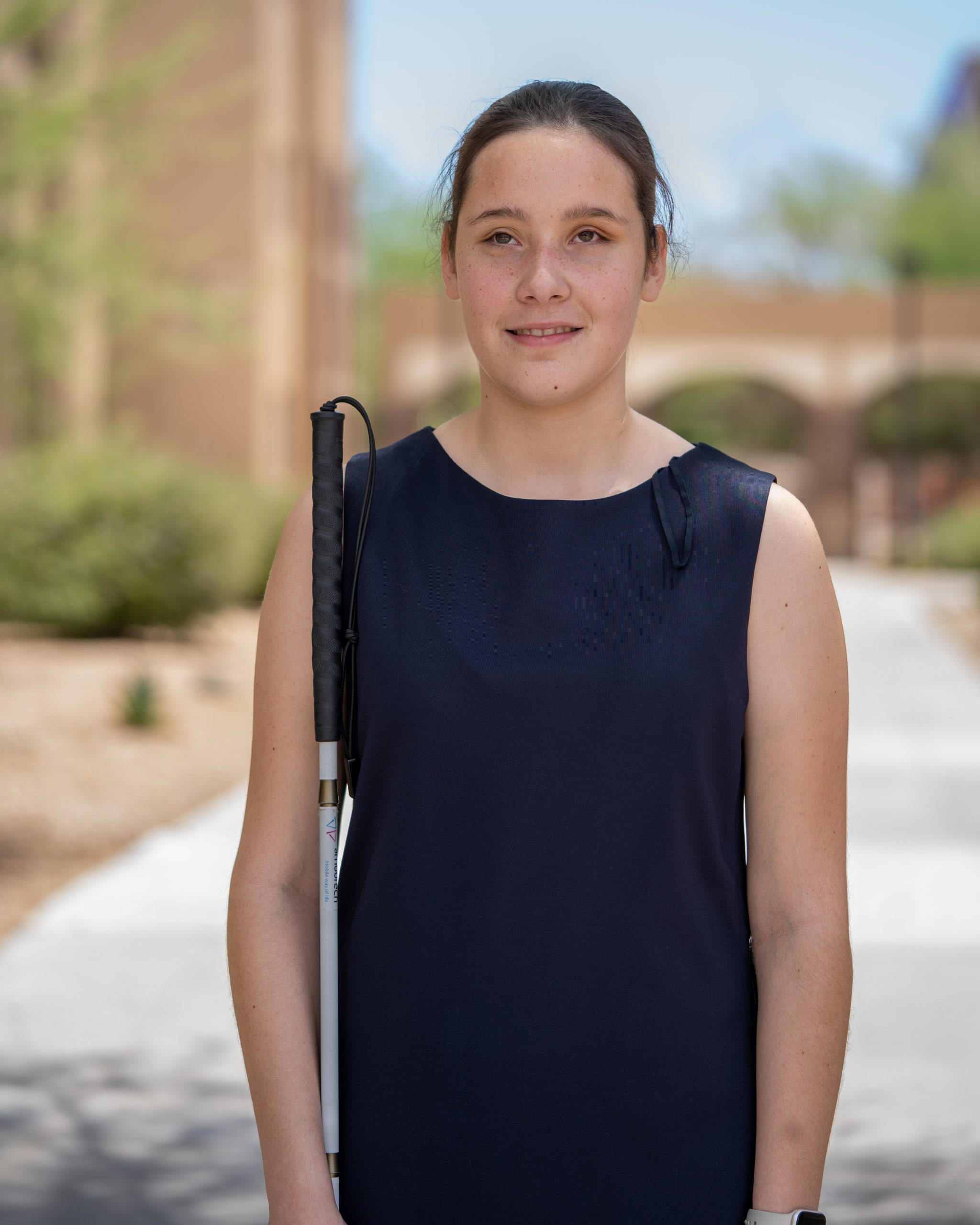 Young girl in a formal black dress, holding a white cane, smiles for her headshot.