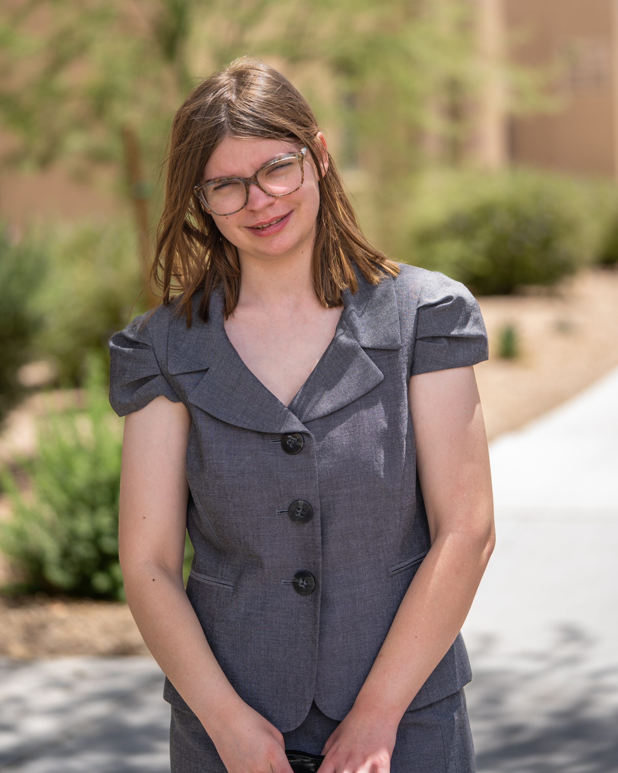 Teenage girl wearing glasses and a brown formal dress smiles for her headshot.
