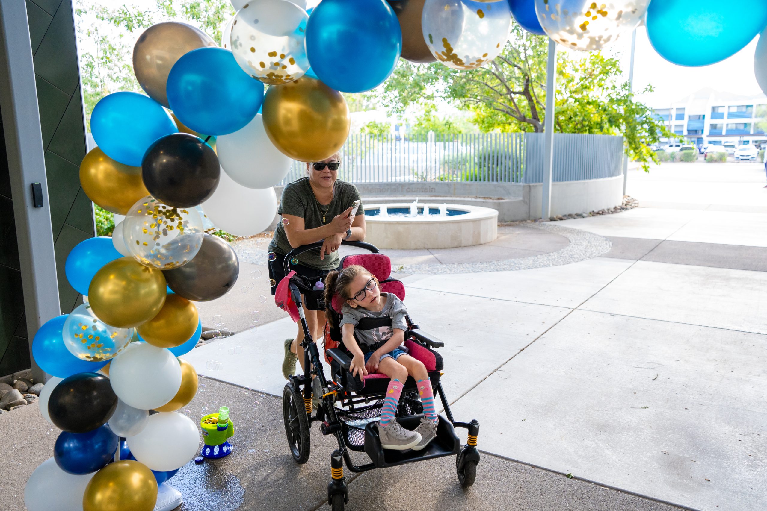 Mother and daughter smile as they walk through the balloon arch