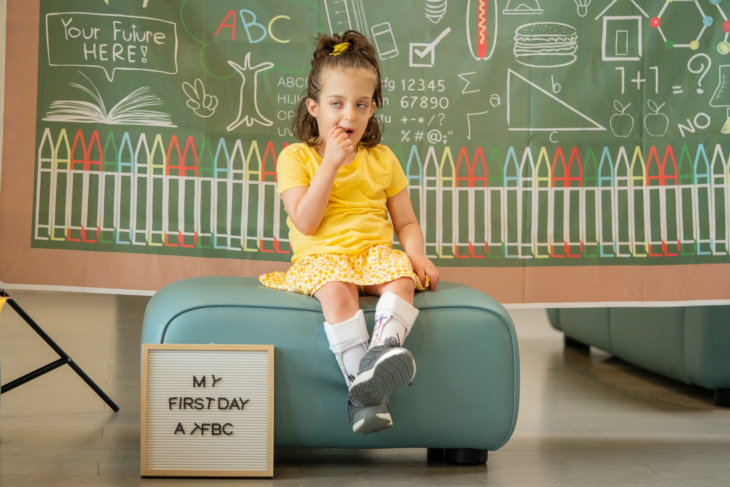 A young girl in a bright yellow outfit sits in front of a colorful, vibrant background.