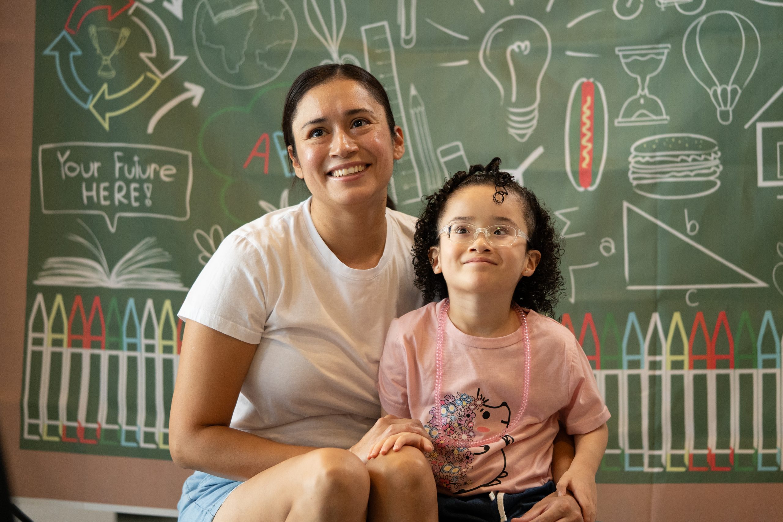A mother and daughter look up at the camera and smile