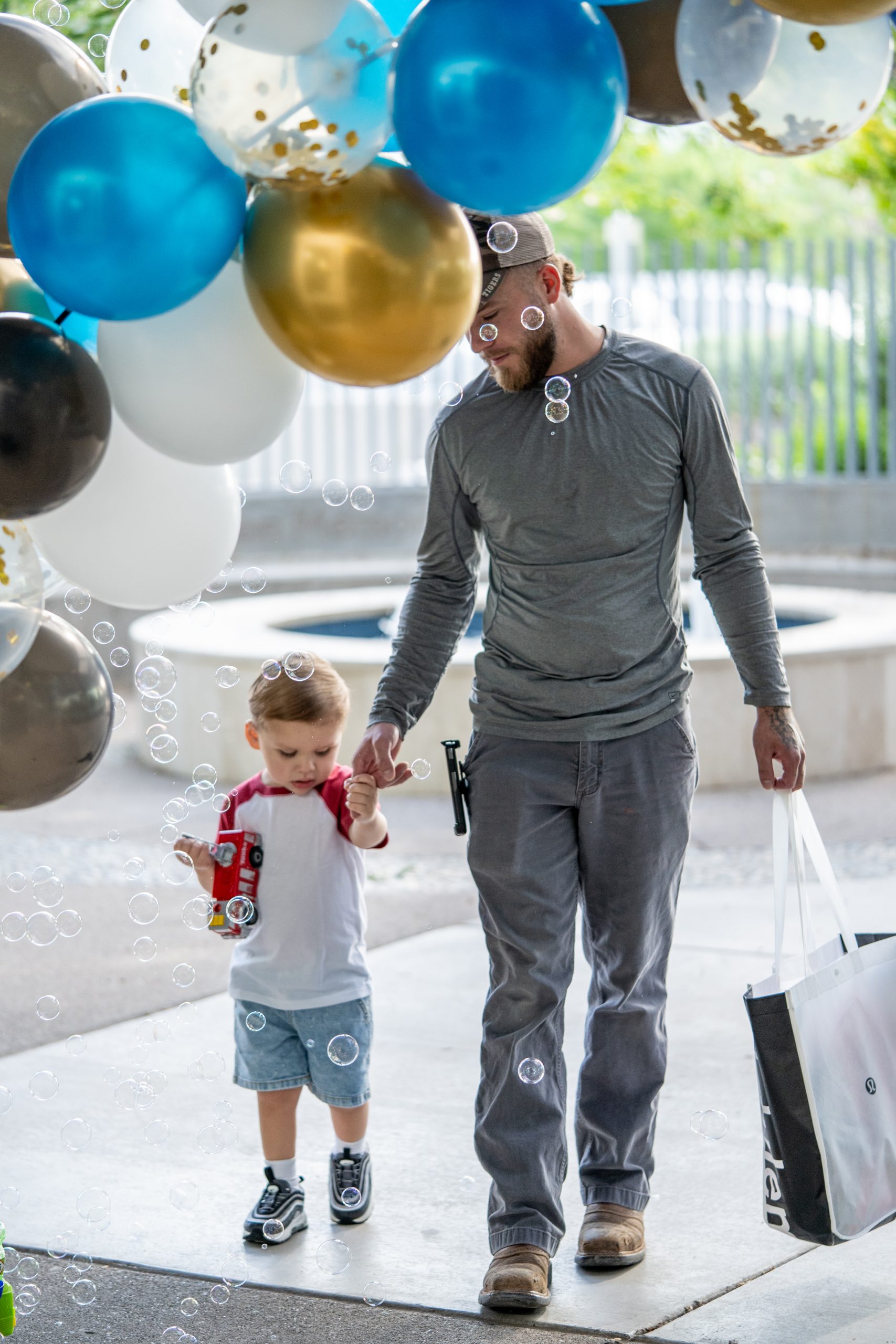 A father and son walk through a balloon arch and bubbles for the first day of school.