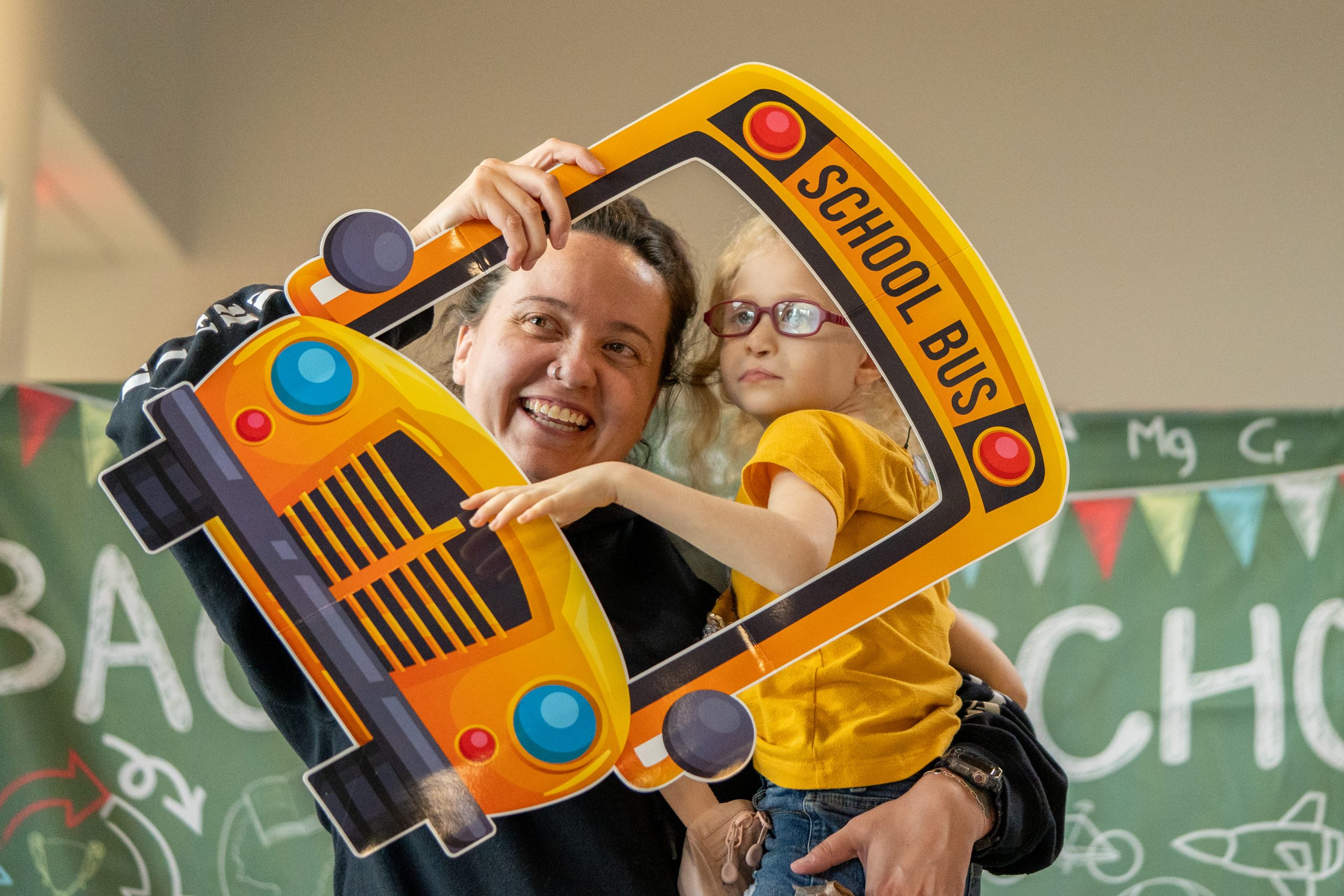 A mother and daughter smile as they pose through a school bus frame prop.