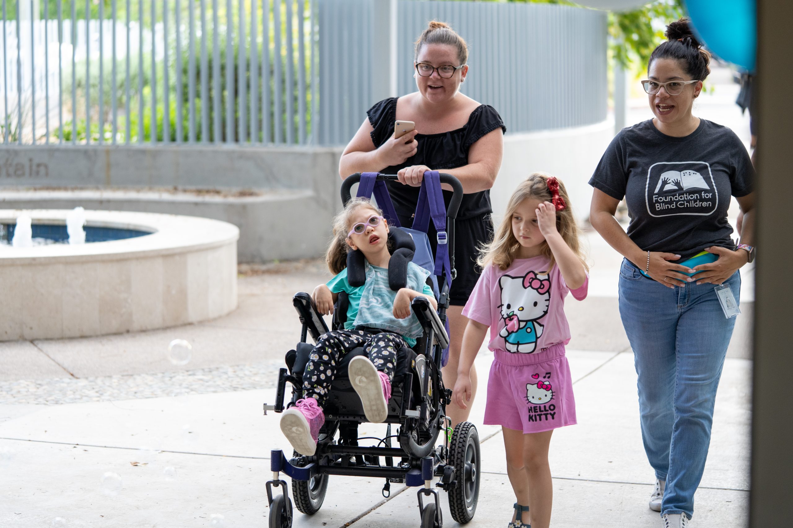 A mother and her children walk through a balloon arch alongside a paraeducator