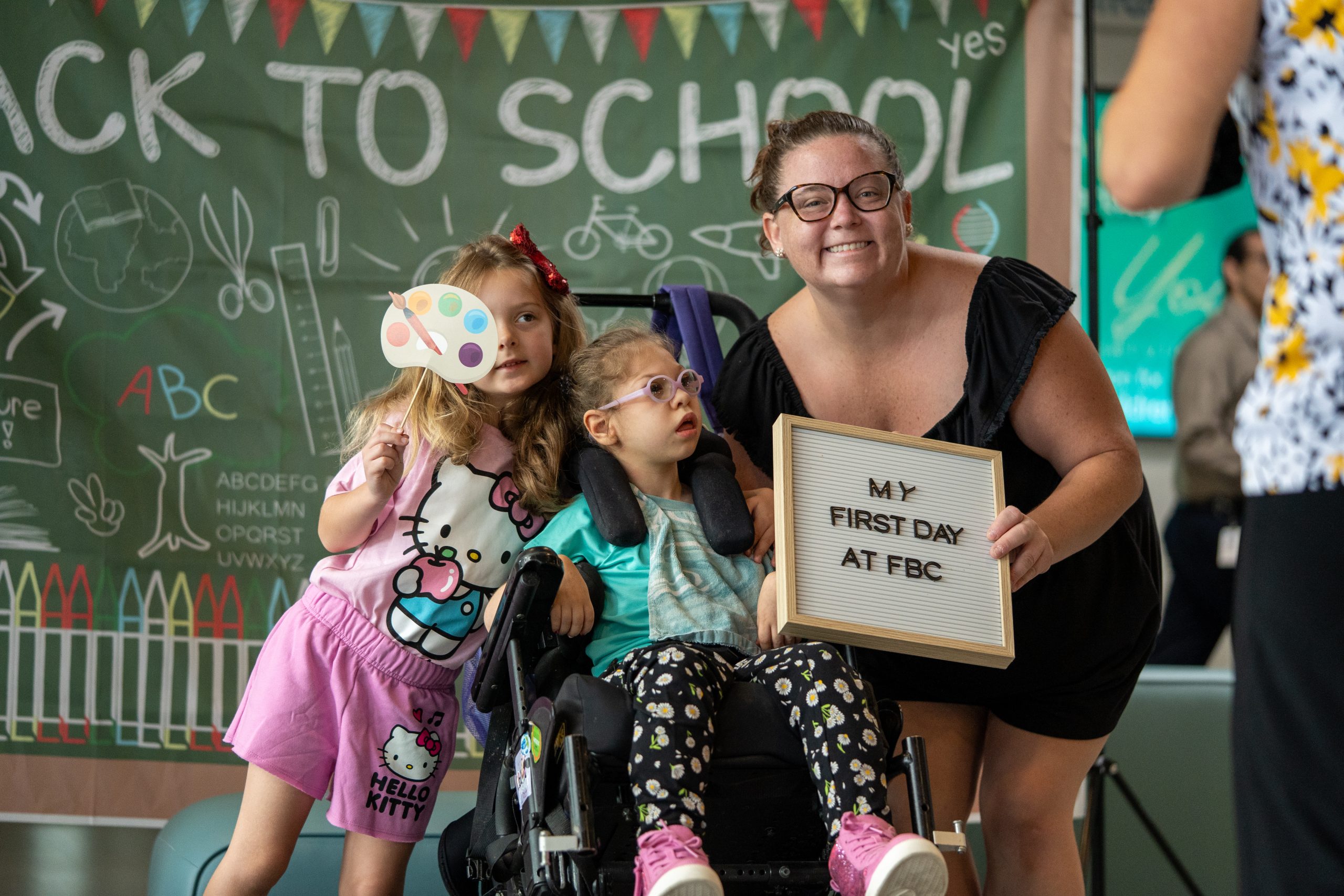 "A mother and her two daughters smile at the camera while holding photo props at FBC's first day of school.