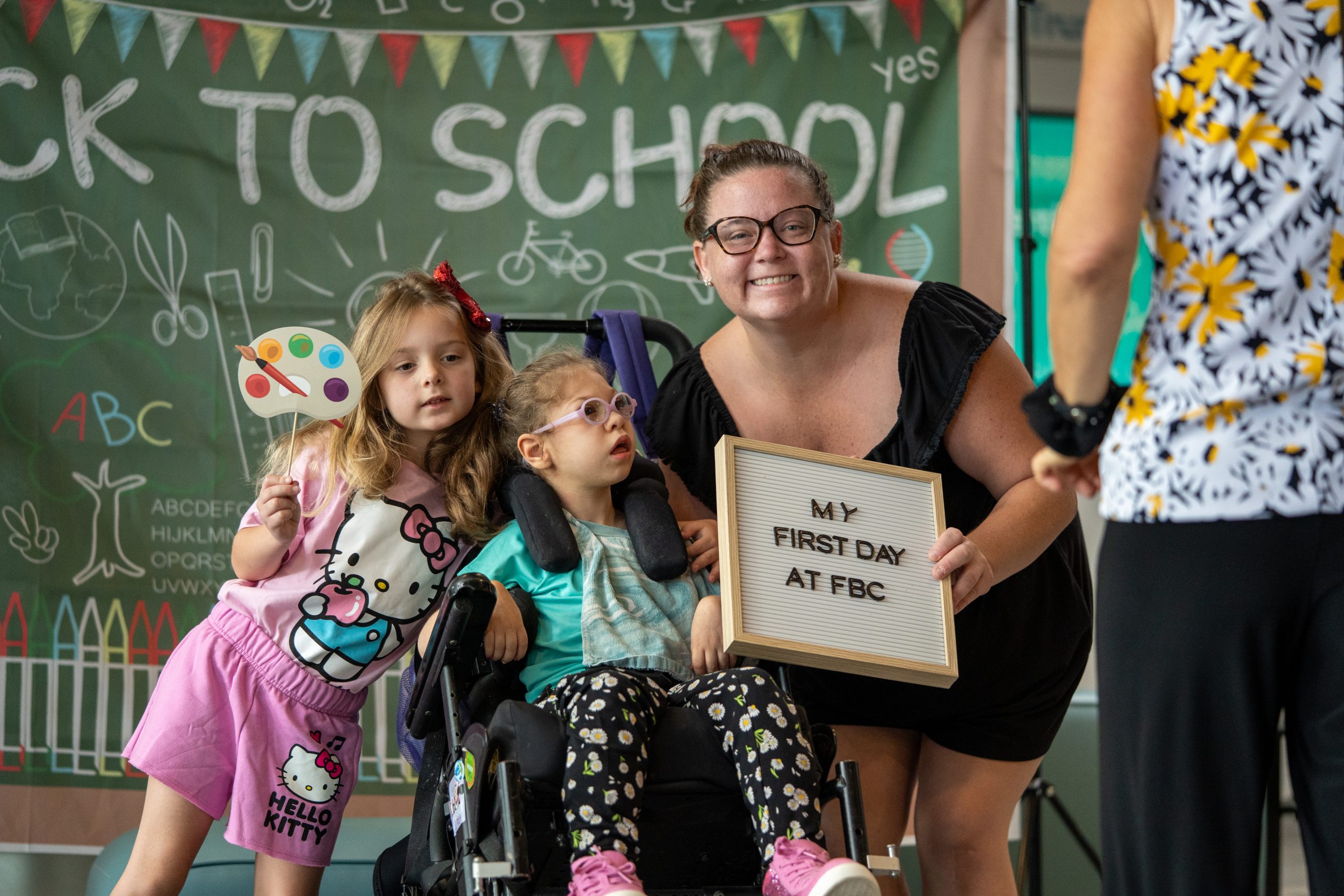 A mother and her two daughters smile at the camera while holding photo props at FBC's first day of school.