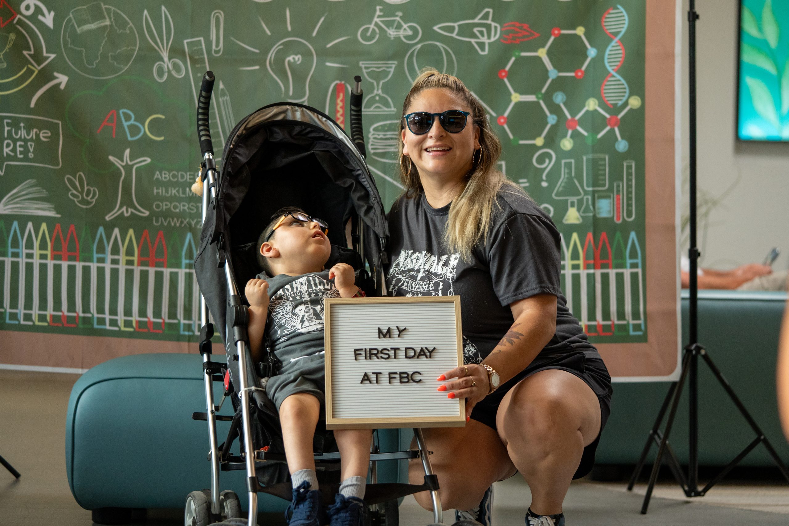 A woman wearing dark glasses smiles at the camera with a little boy by her side.
