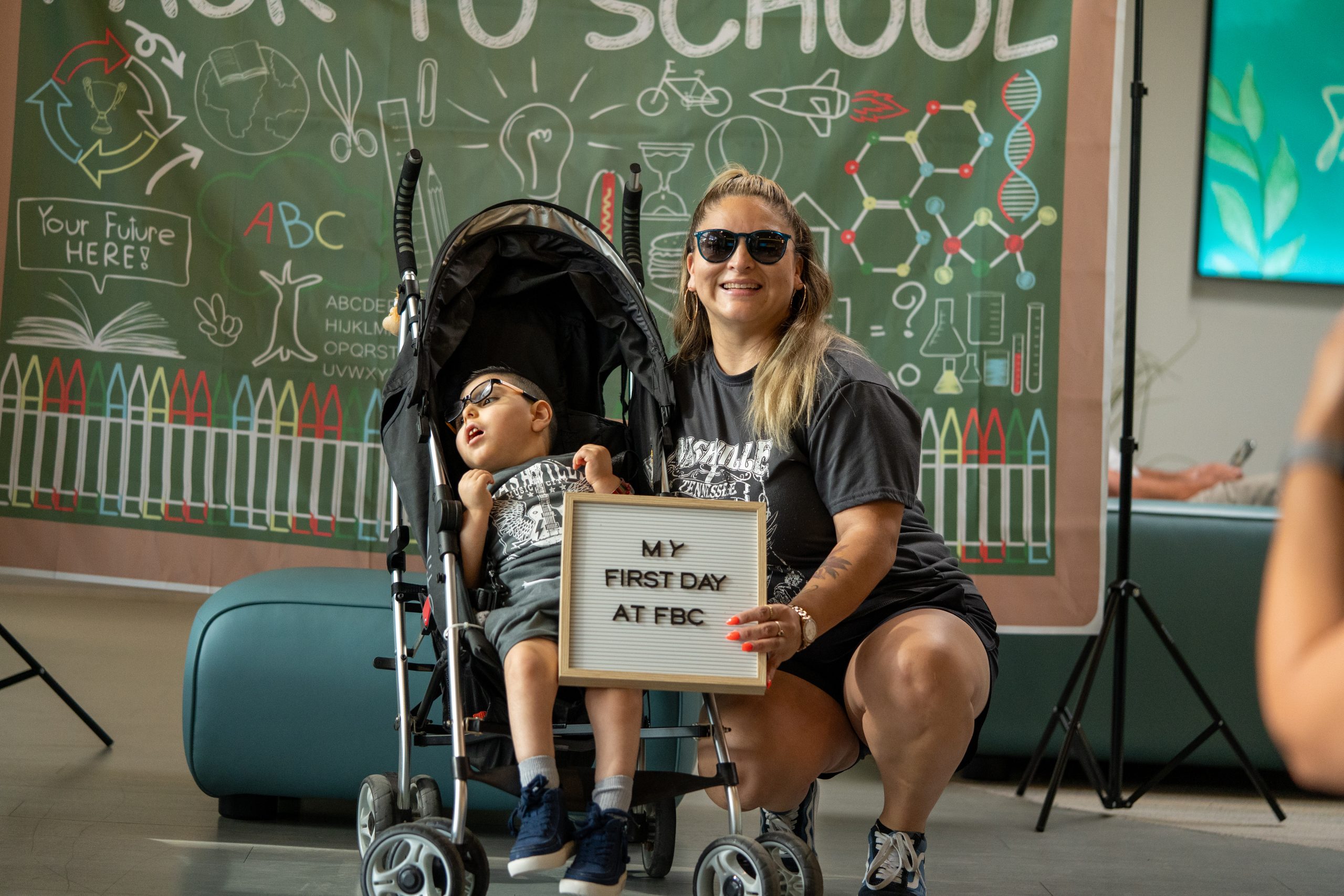 A woman wearing dark glasses smiles at the camera with a little boy by her side.